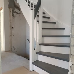 FPHU „MARKUZ” Marcin Kuzara - Białe schody drewniane z szarymi stopniami w trakcie montażu, widoczne niedokończone ściany i podłoga.