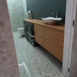 Nowoczesna łazienka z drewnianym blatem, umywalką w kształcie muszli, pralką i płytkami lastryko.