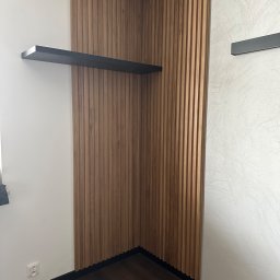 FPHU „MARKUZ” Marcin Kuzara - Drewniane lamele ścienne w rogu pokoju, z czarną półką i ciemną podłogą, uzupełniające minimalistyczny design wnętrza.