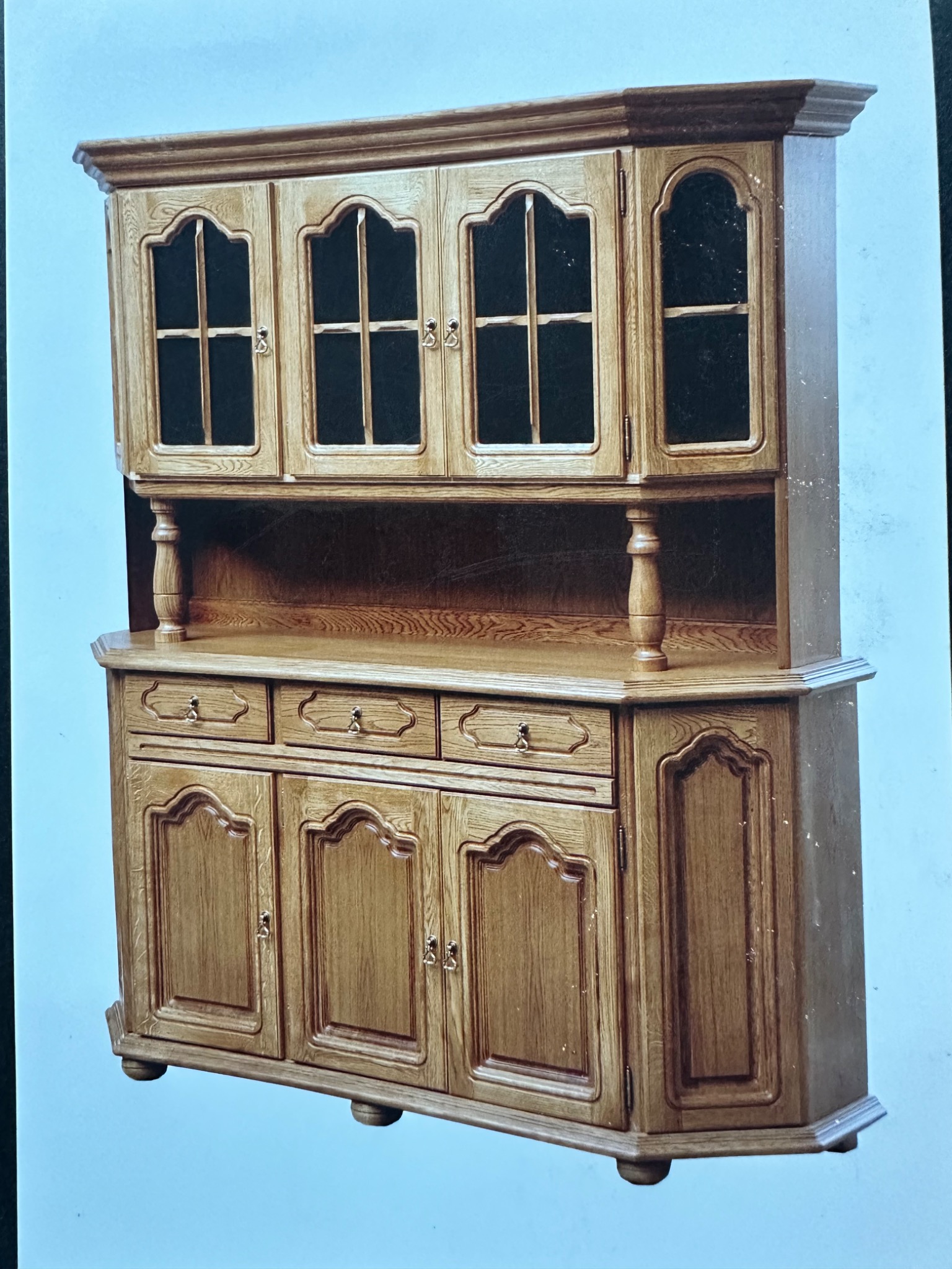 Drewniany kredens w stylu retro z przeszklonymi szafkami i szufladami, widoczny na jasnym tle. Charakterystyczne zdobienia i wykończenie.