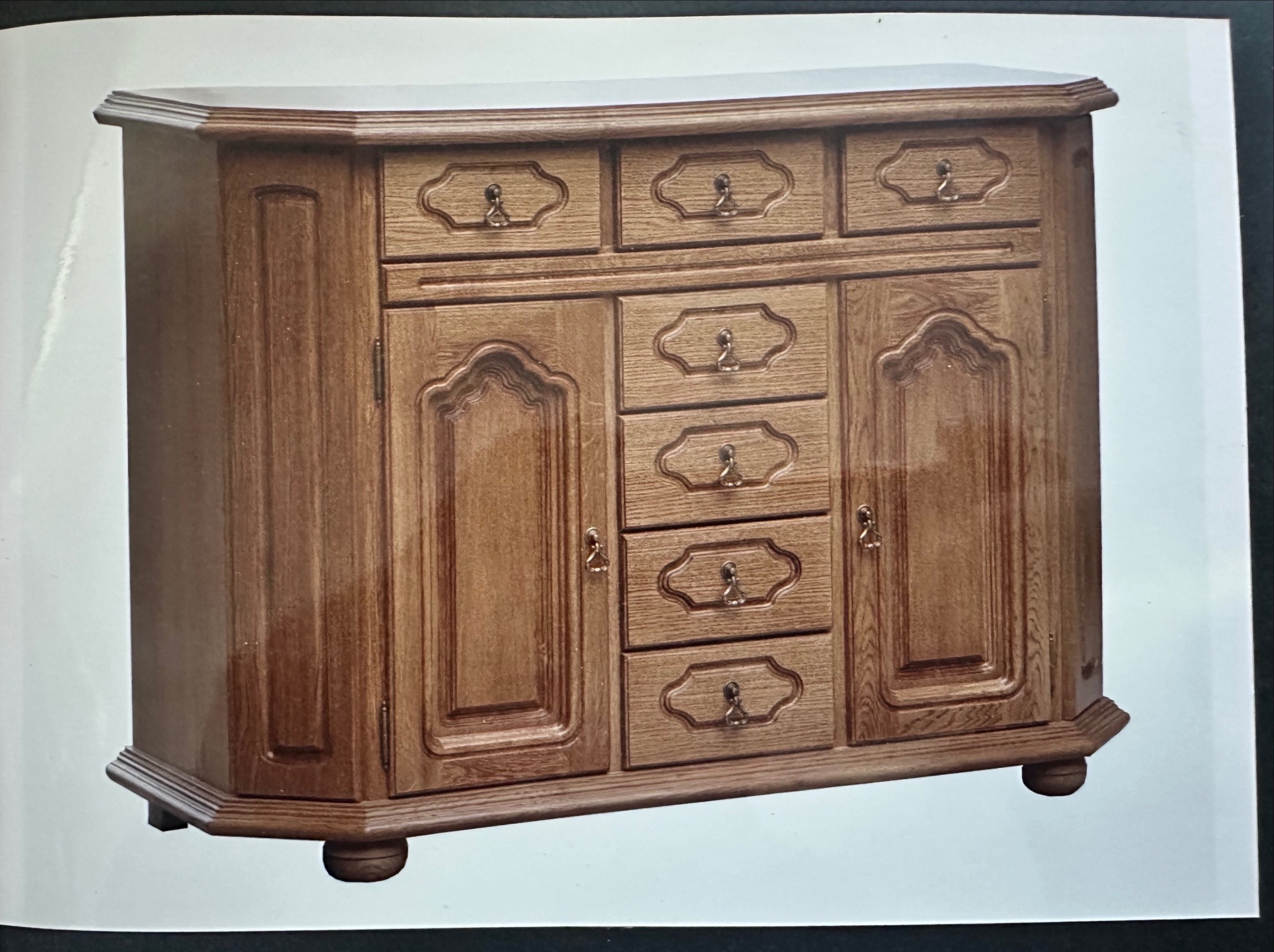 Drewniana komoda z szufladami i szafkami, w stylu retro, z ozdobnymi uchwytami i frezowanymi frontami, na toczonych nóżkach. Wykończenie w ciepłym odcieniu dębu.