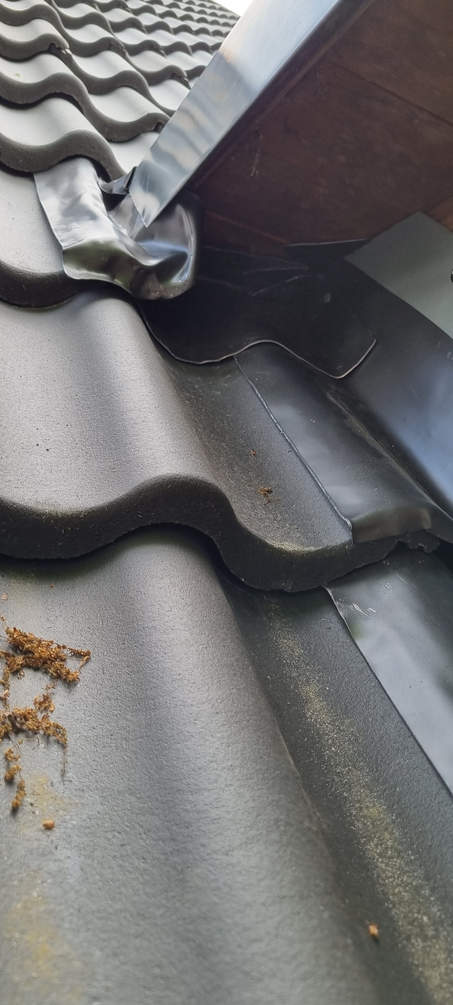 Szczegółowe ujęcie czarnych dachówek ceramicznych z widocznym systemem odprowadzania wody deszczowej, zakończonym elastycznym kołnierzem uszczelniającym.