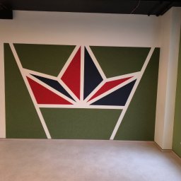 Grand-Bud Sofiia Yakobchuk - Geometryczny wzór w kształcie korony z czerwonymi i granatowymi elementami na zielonym tle, otoczony białymi liniami na białej ścianie w biurze.