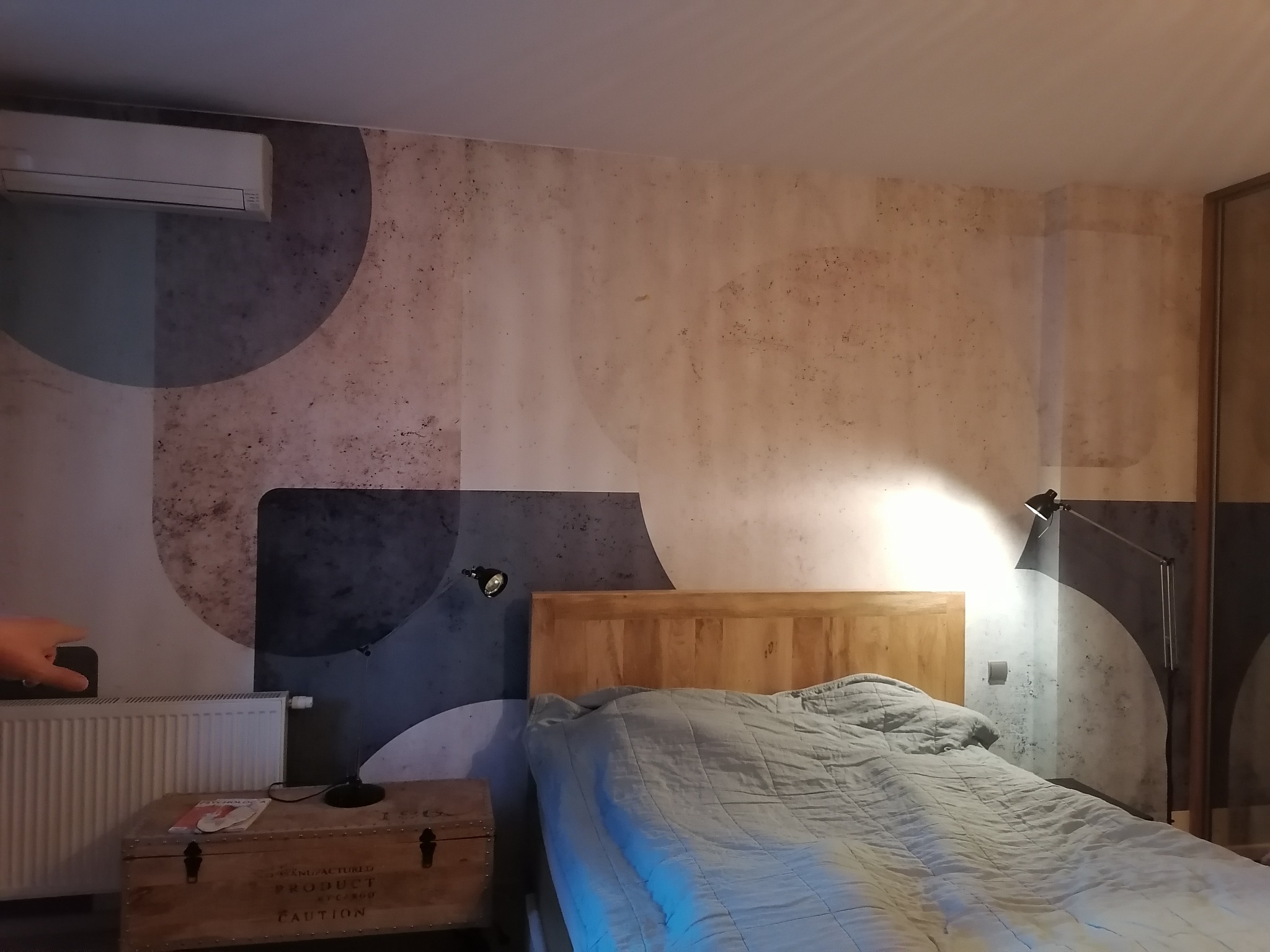 Sypialnia z łóżkiem, grzejnikiem i ścianą z dekoracyjną tapetą w geometryczne wzory, oświetlona lampką nocną