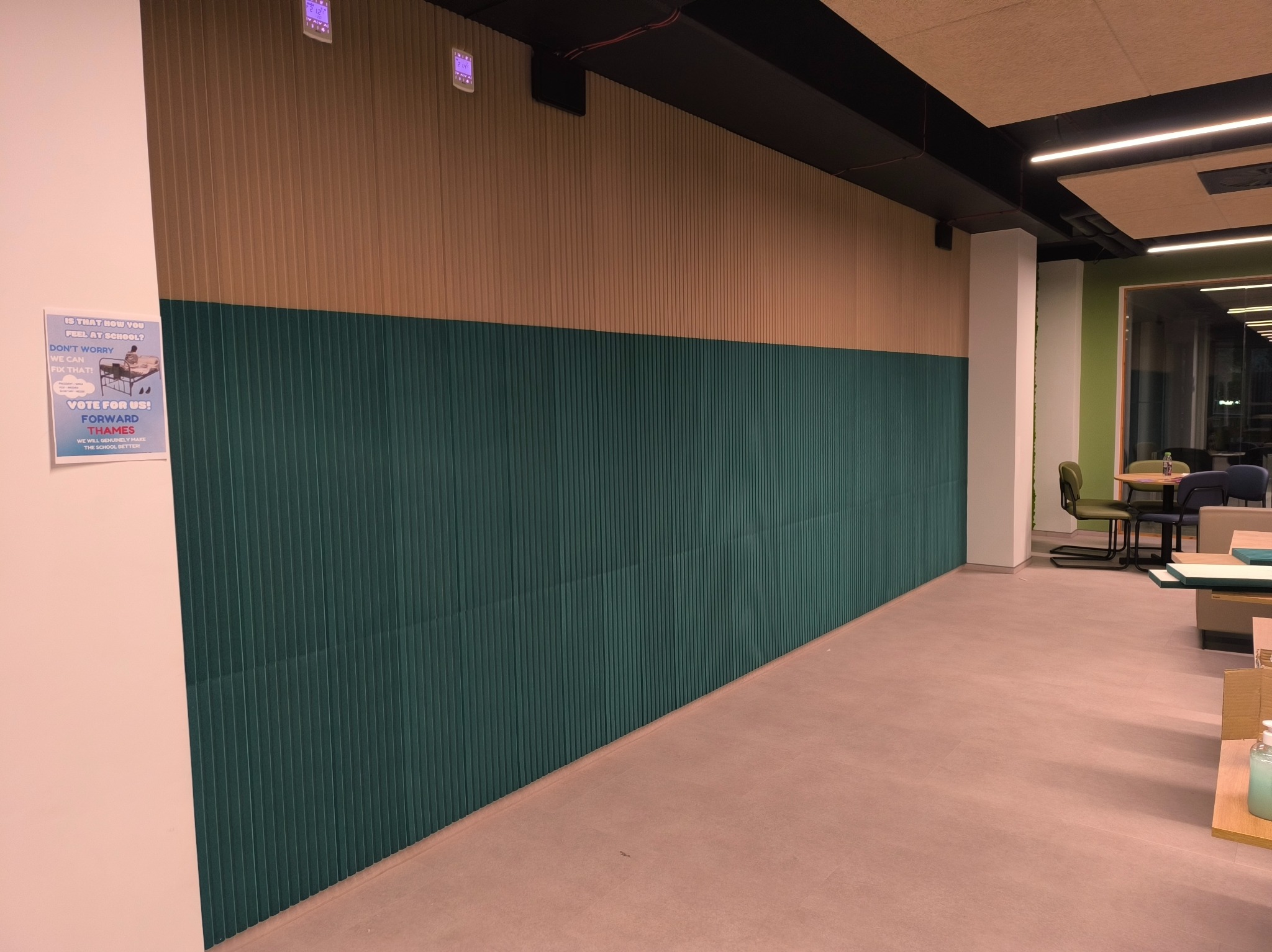 Wnętrze biurowe w Warszawie z pionowymi panelami ściennymi w kolorze zielonym i beżowym, widoczne również elementy wyposażenia takie jak stoły i krzesła.