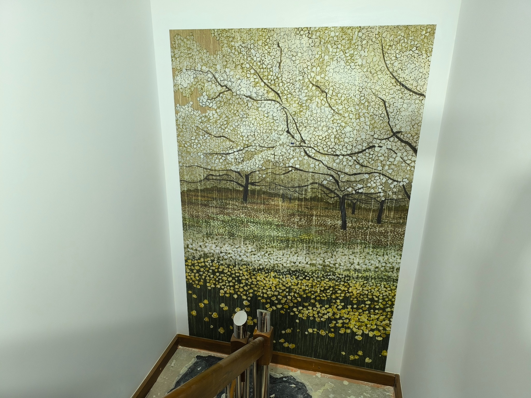 Nowoczesna tapeta z motywem kwitnących drzew na ścianie w klatce schodowej, widok z góry na fragment schodów z metalową balustradą.