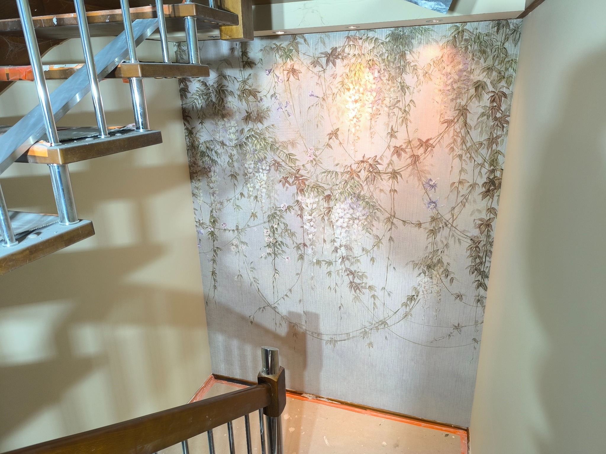 Ściana z tapetą w motywy kwitnącej glicynii, widok z dołu schodów z metalowo-drewnianą konstrukcją.