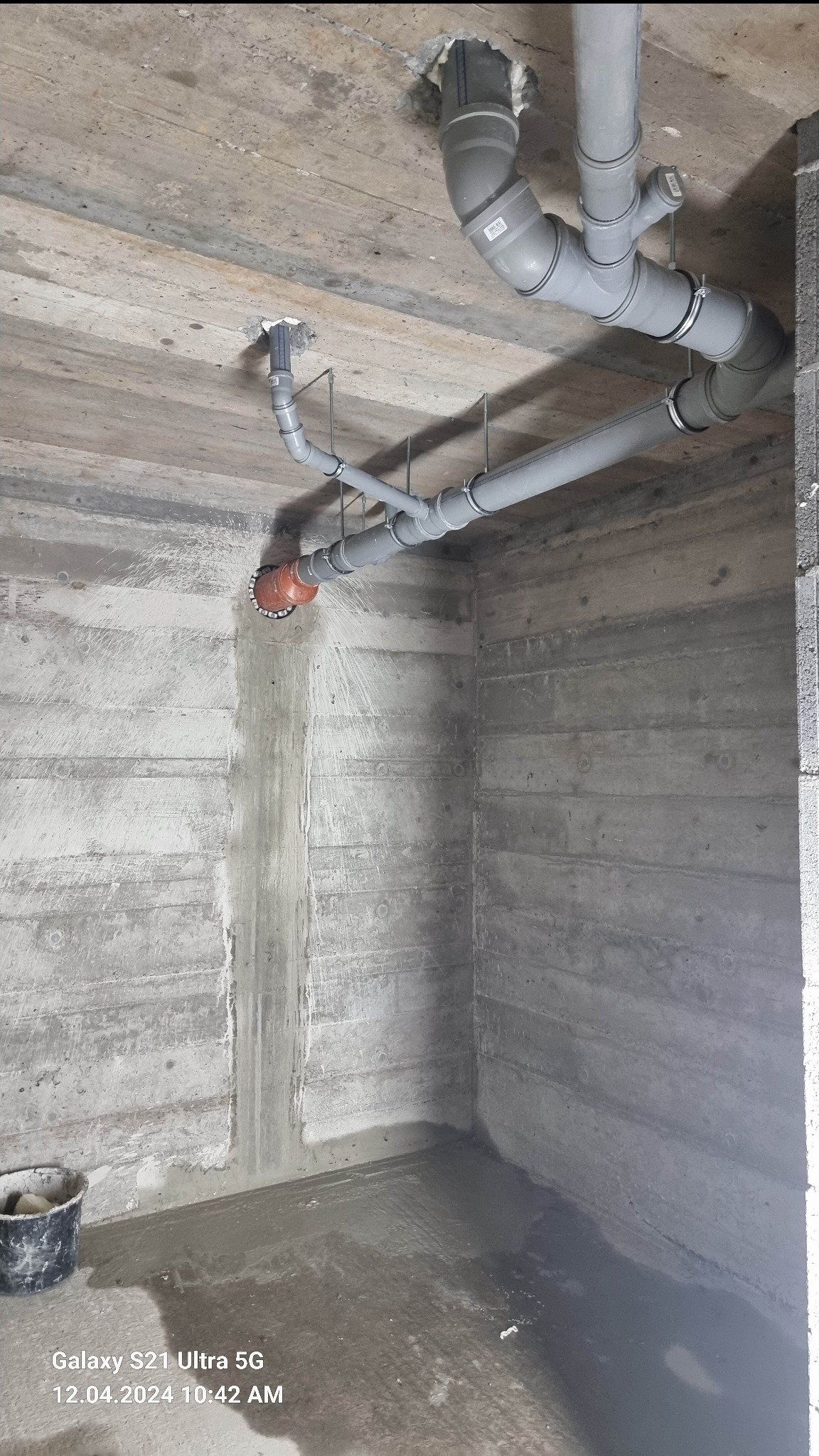 Szare rury kanalizacyjne zamontowane pod betonowym sufitem w surowym pomieszczeniu, widoczne mocowania i uszczelnienia.