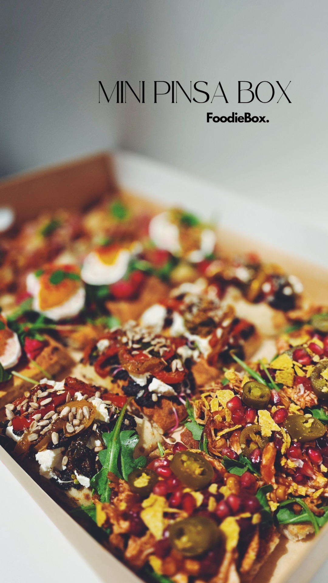 Mini pinsa box od FoodieBox: różnorodne, kolorowe przekąski na cieście, z jajkiem, warzywami i owocami, ułożone w kartonowym pudełku.
