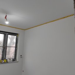 Stol-Lux - Pokój po szpachlowaniu i malowaniu na biało, zabezpieczony żółtą taśmą malarską przy suficie, okno zakryte folią ochronną.
