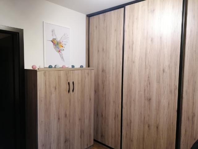 Szafa przesuwna z frontami w kolorze jasnego drewna z czarnymi obramowaniami, obok szafka z ozdobami i obrazkiem kolibra.