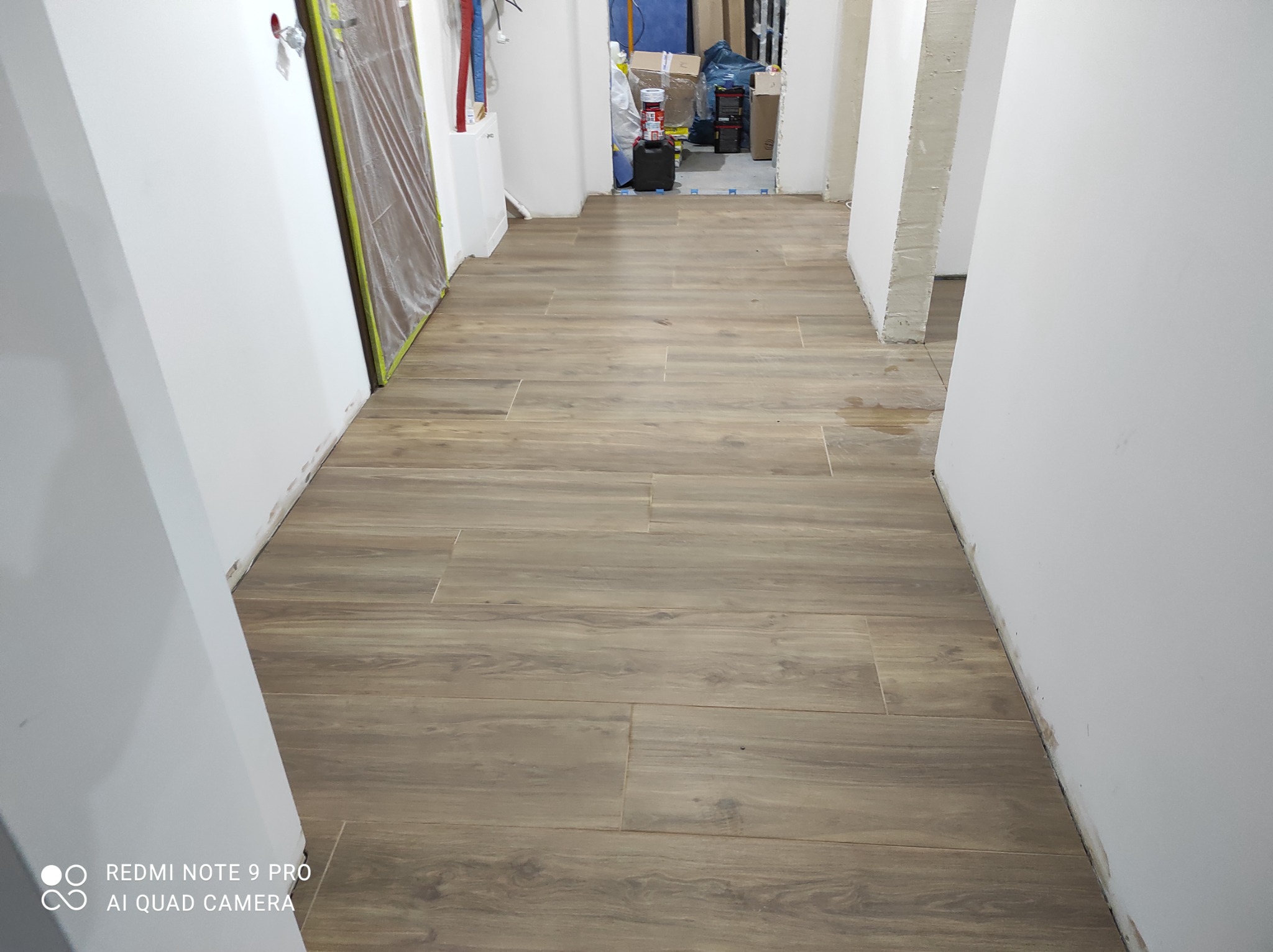 Ułożone brązowe panele podłogowe w korytarzu w trakcie remontu, widoczne przygotowane ściany do malowania oraz zabezpieczone drzwi w Lubinie.
