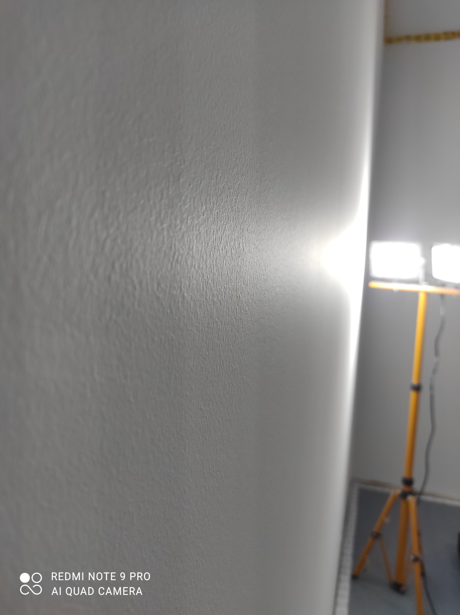 Świeżo wyszpachlowana ściana oświetlona lampą roboczą na statywie, widoczne drobne nierówności faktury.