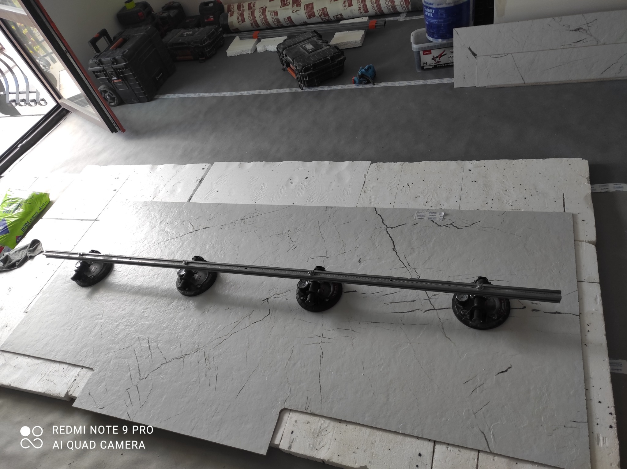 Płyty imitujące marmur z przyssawkami do przenoszenia, przygotowane do montażu, widoczne narzędzia i materiały budowlane w tle.