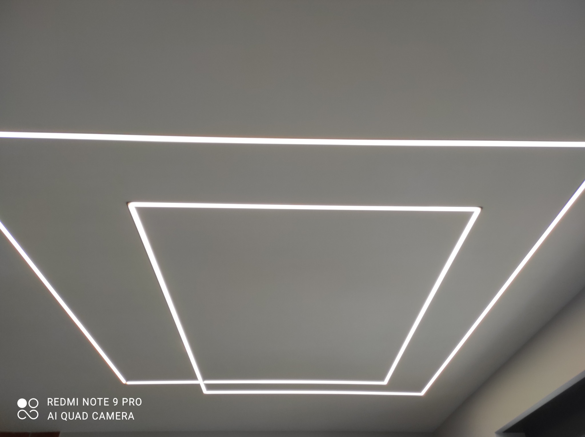 Nowoczesne oświetlenie sufitowe z liniowymi lampami LED ułożonymi w geometryczny wzór kwadratu i linii, tworzące minimalistyczny design.