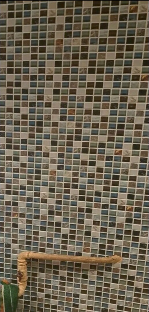 Ściana łazienki wyłożona mozaiką z drobnych, kwadratowych płytek w odcieniach beżu, brązu i błękitu; widoczny fragment drewnianego relingu na ręczniki.