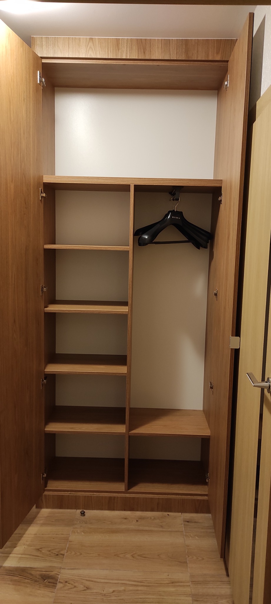 Otwarta szafa wnękowa z jasnego drewna z półkami po lewej stronie i wieszakiem na ubrania marki Vistula po prawej stronie.