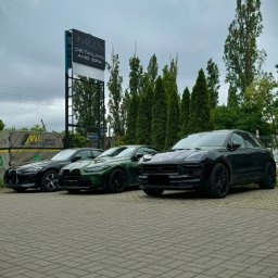 Hills detailing and SPA - Auto detailing Poznań, Powłoka ceramiczna, Folia PPF - Rząd trzech samochodów: czarny BMW, zielony BMW M4 i czarny Porsche Macan, stojących na brukowanym parkingu przed salonem detailingowym Hills Detailing and Spa pod pochmurnym niebem.
