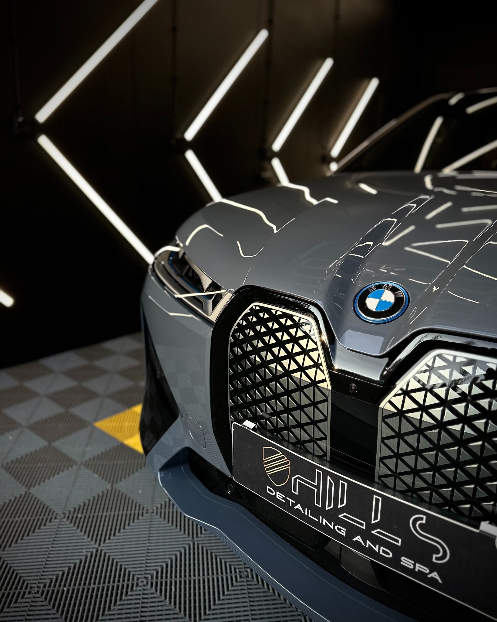 Szary samochód BMW iX z bliska, po nałożeniu folii ochronnej, widoczne logo firmy detailingowej na tle charakterystycznego grilla i oświetlenia LED.