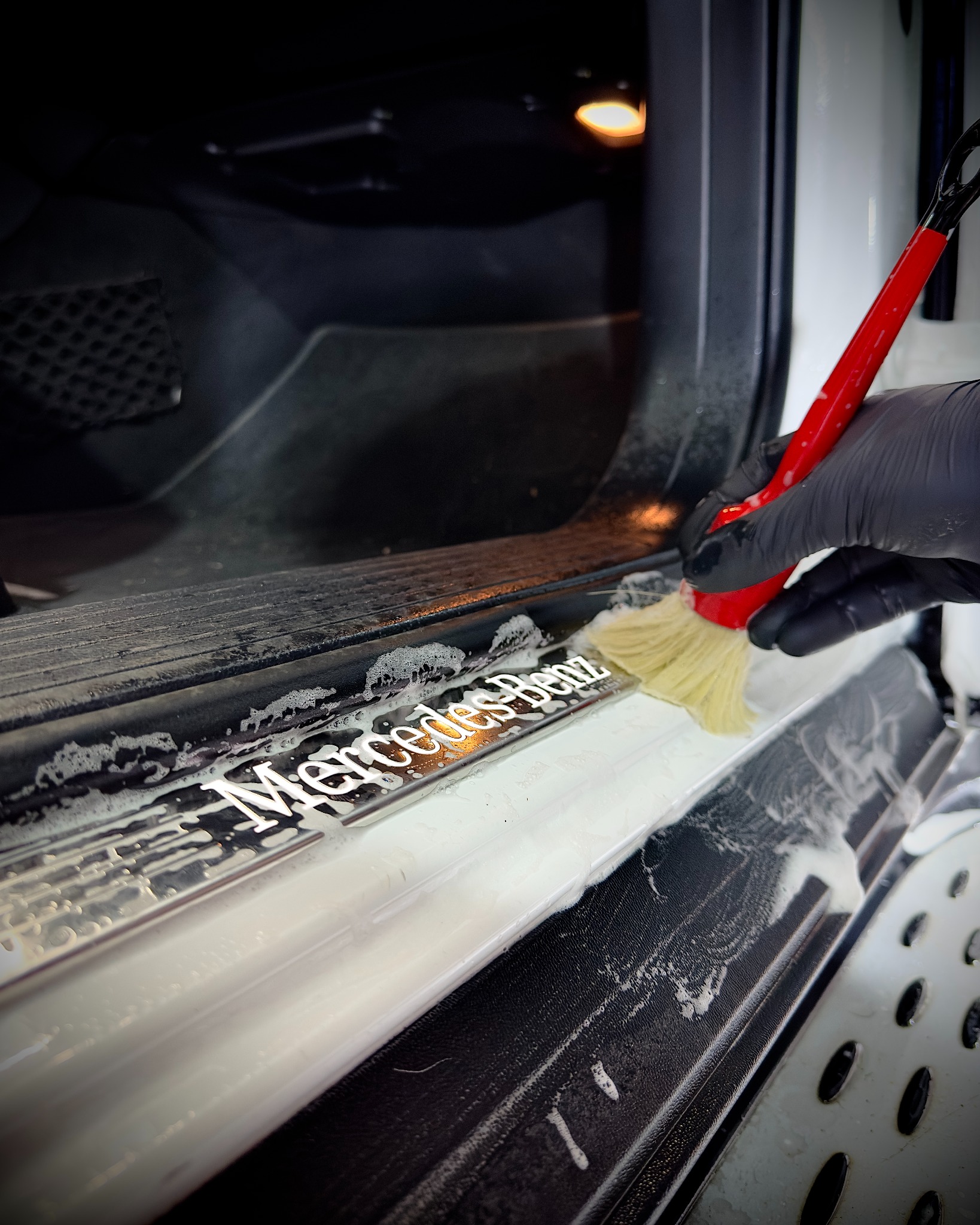 Czyszczenie progu samochodu marki Mercedes-Benz szczoteczką z miękkim włosiem, widoczne ślady piany czyszczącej.