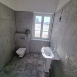 Wykończona łazienka w szarościach z heksagonalną podłogą, wiszącą toaletą i umywalką na postumencie, widok na zaśnieżone pole przez okno.