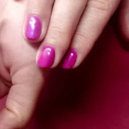 Dłoń z pomalowanymi na intensywny róż paznokciami, jeden paznokieć z efektem połysku.