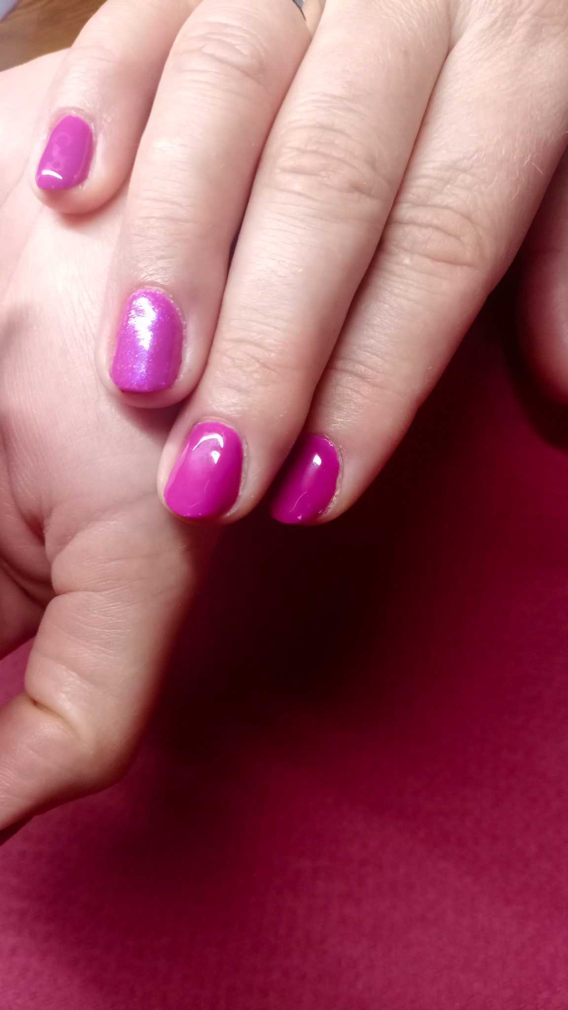 Dłoń z pomalowanymi na intensywny róż paznokciami, jeden paznokieć z efektem połysku.