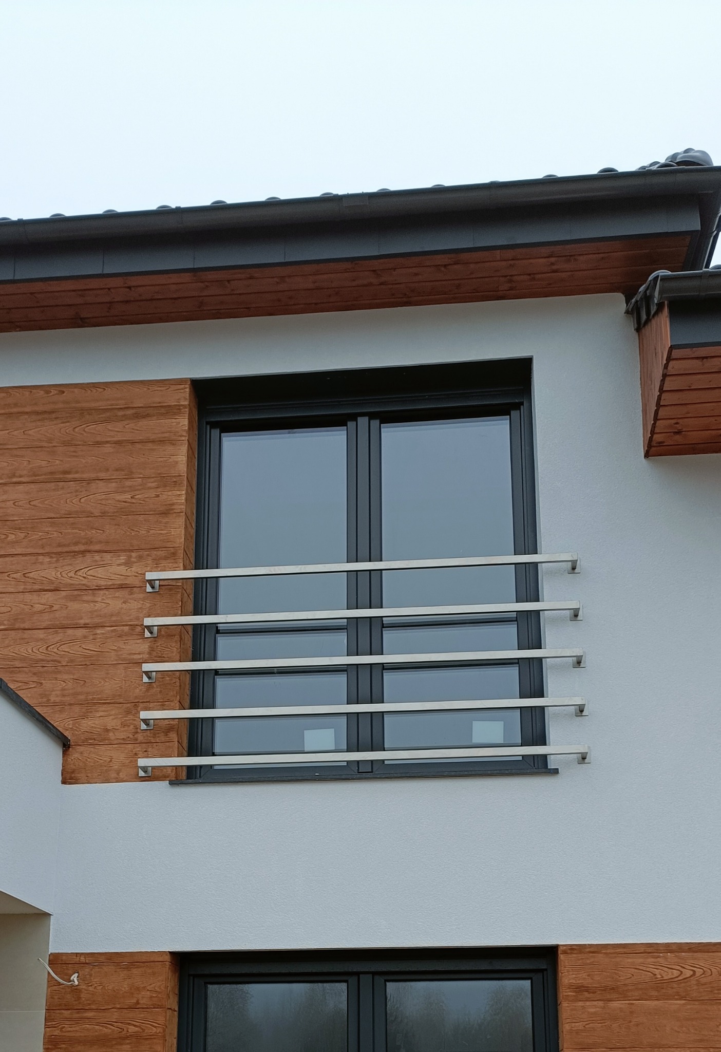 Nowoczesna, minimalistyczna balustrada okienna ze stali nierdzewnej, z poziomymi profilami i kwadratowymi mocowaniami, zamontowana na balkonie w Bydgoszczy, na tle białej elewacji z elementami...