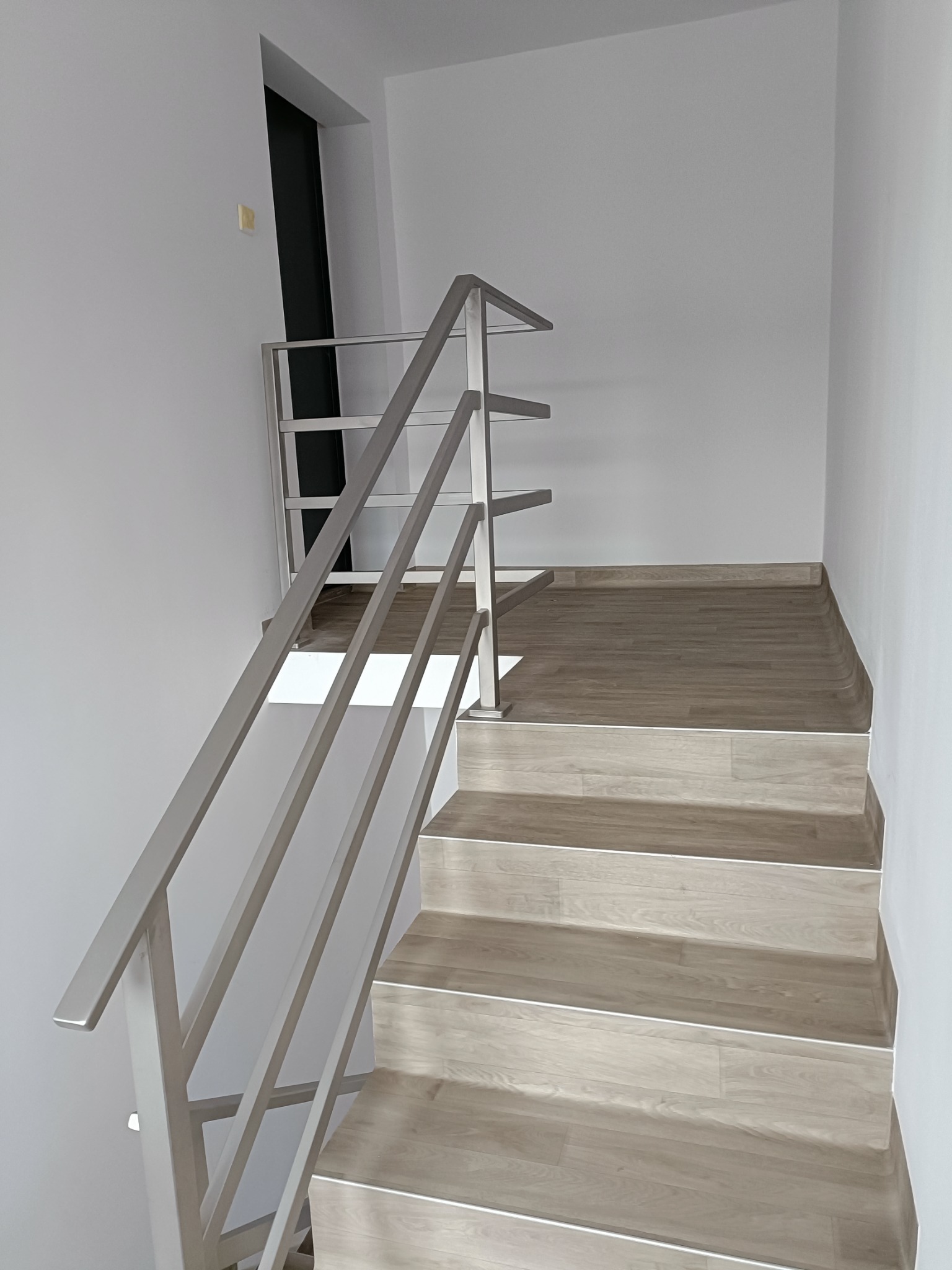 Wewnętrzne schody z drewnopodobnymi stopniami i prostą, nowoczesną balustradą ze stali nierdzewnej z poziomymi wypełnieniami, widziane od dołu.