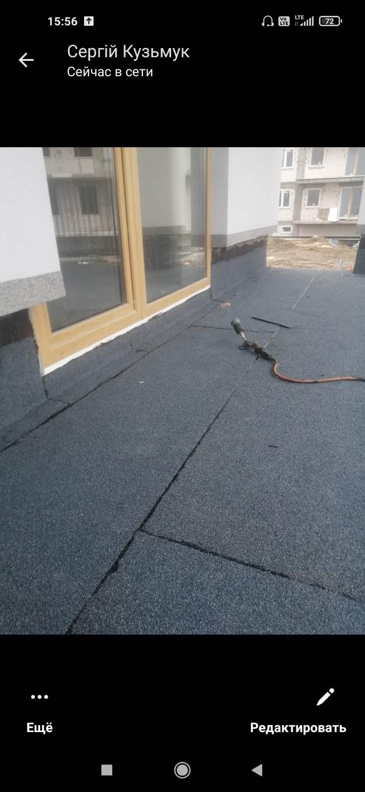 Nowe pokrycie dachu papą termozgrzewalną w trakcie prac wykończeniowych, widoczny palnik dekarski i okno dachowe. W tle budynek w stanie surowym.