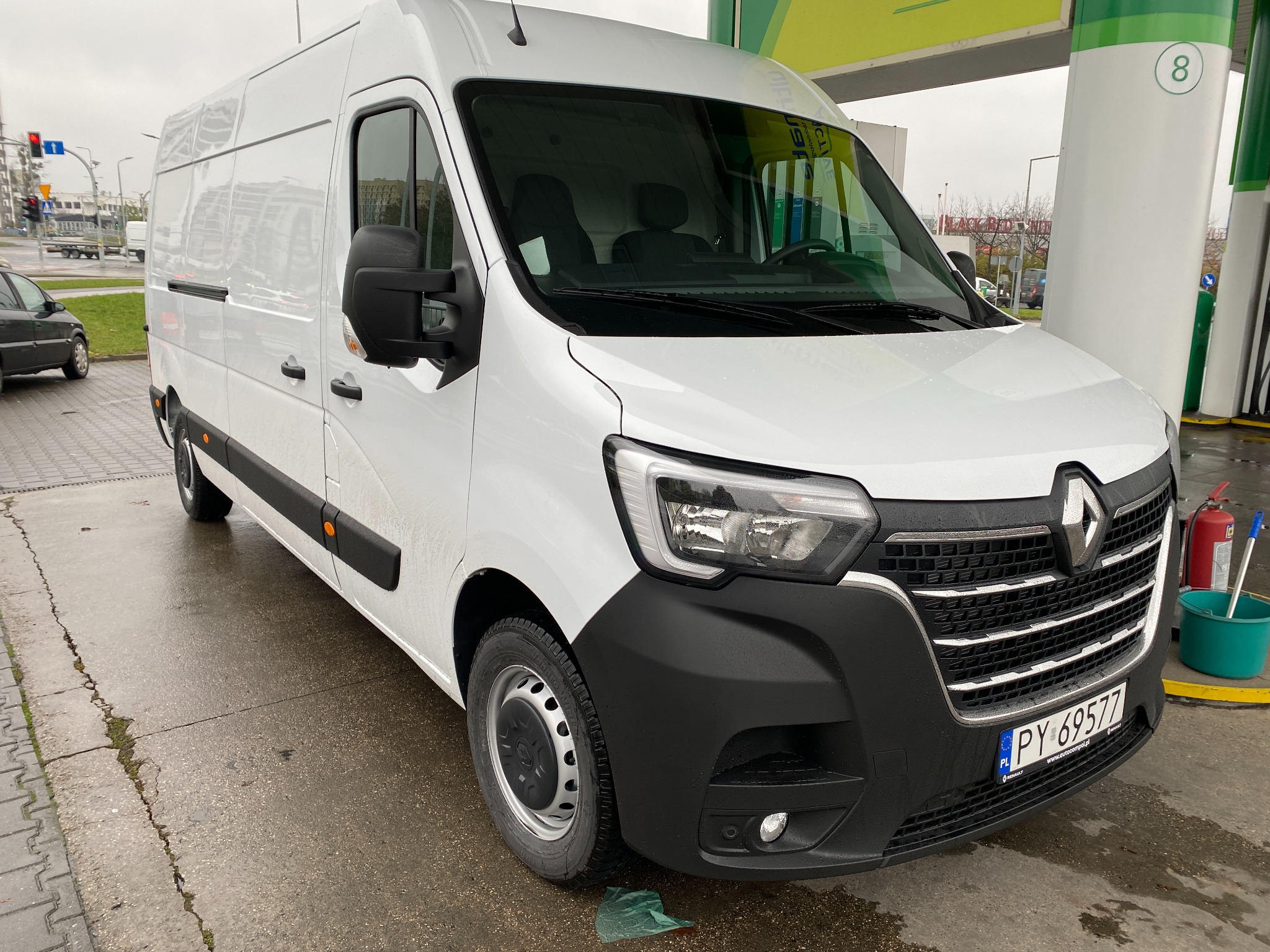 Biały samochód dostawczy Renault Master zaparkowany na stacji benzynowej BP, widok z przodu na mokrym asfalcie.