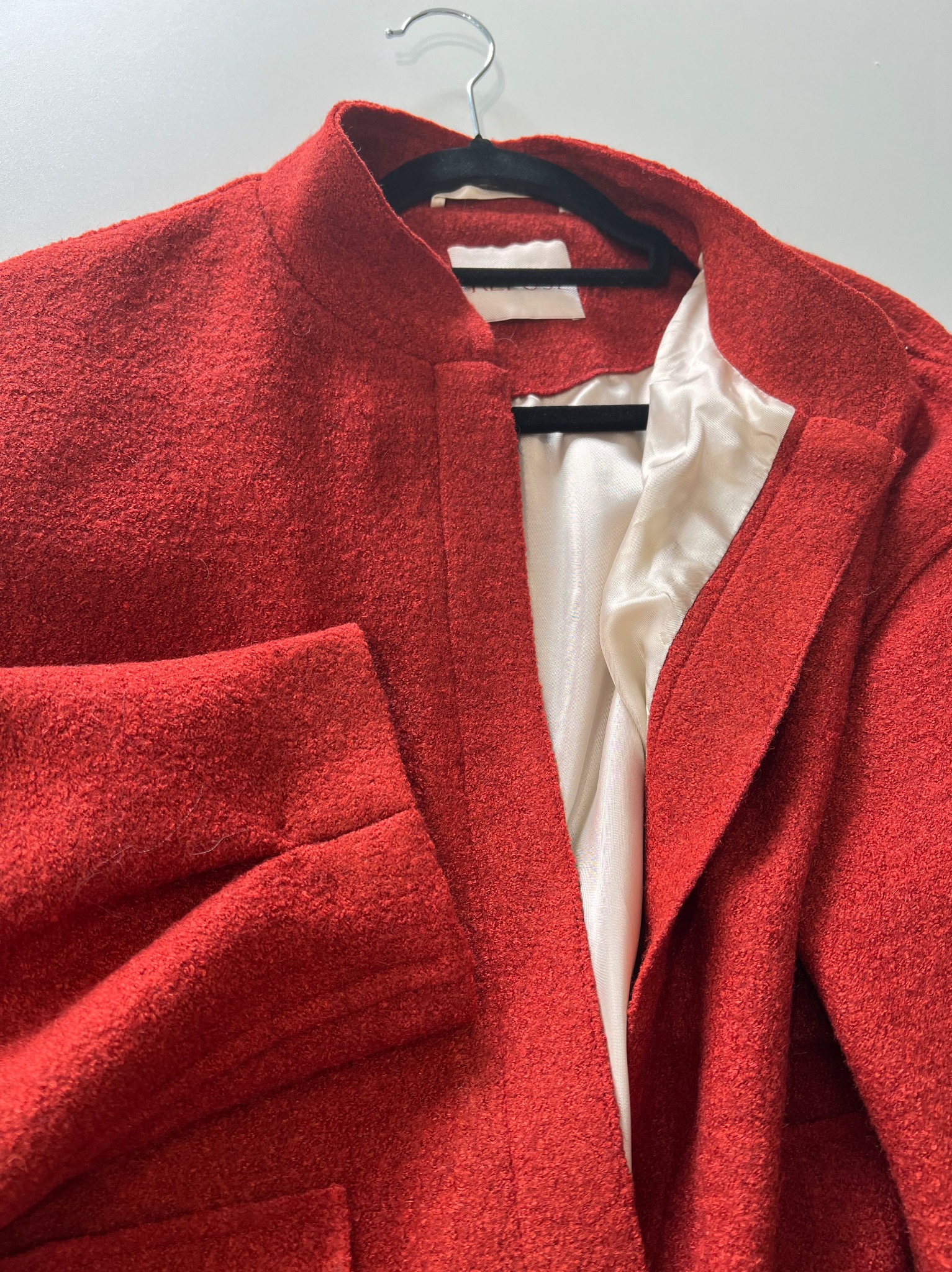 Czerwony, teksturowany płaszcz damski z satynową podszewką, zawieszony na czarnym wieszaku, sfotografowany z bliska z widocznym detalem faktury materiału.