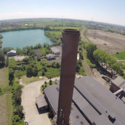 Mega-Net Sp. z o. o. - Widok z drona na ceglany komin przemysłowy, jezioro i pola w tle, widoczne linie energetyczne.