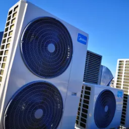 Instalacja kilku jednostek zewnętrznych klimatyzacji marki Midea na dachu budynku, widok z dołu na tle błękitnego nieba.