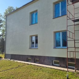 Pro Clean Cezary Woźniak - Budynek po malowaniu elewacji, okna zabezpieczone folią, widoczne rusztowanie. Świeża, jasna elewacja kontrastuje z ciemną podmurówką i zielonym trawnikiem.