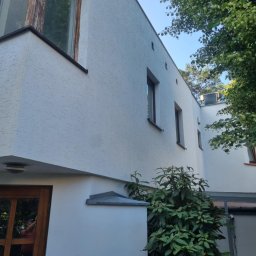Pro Clean Cezary Woźniak - Biała elewacja domu z widocznymi oknami i zielenią. Ujęcie z dołu, podkreślające strukturę tynku i bryłę budynku w słoneczny dzień.