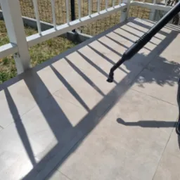 Czyszczenie jasnych płytek na tarasie parownicą, widoczne białe balustrady w tle.