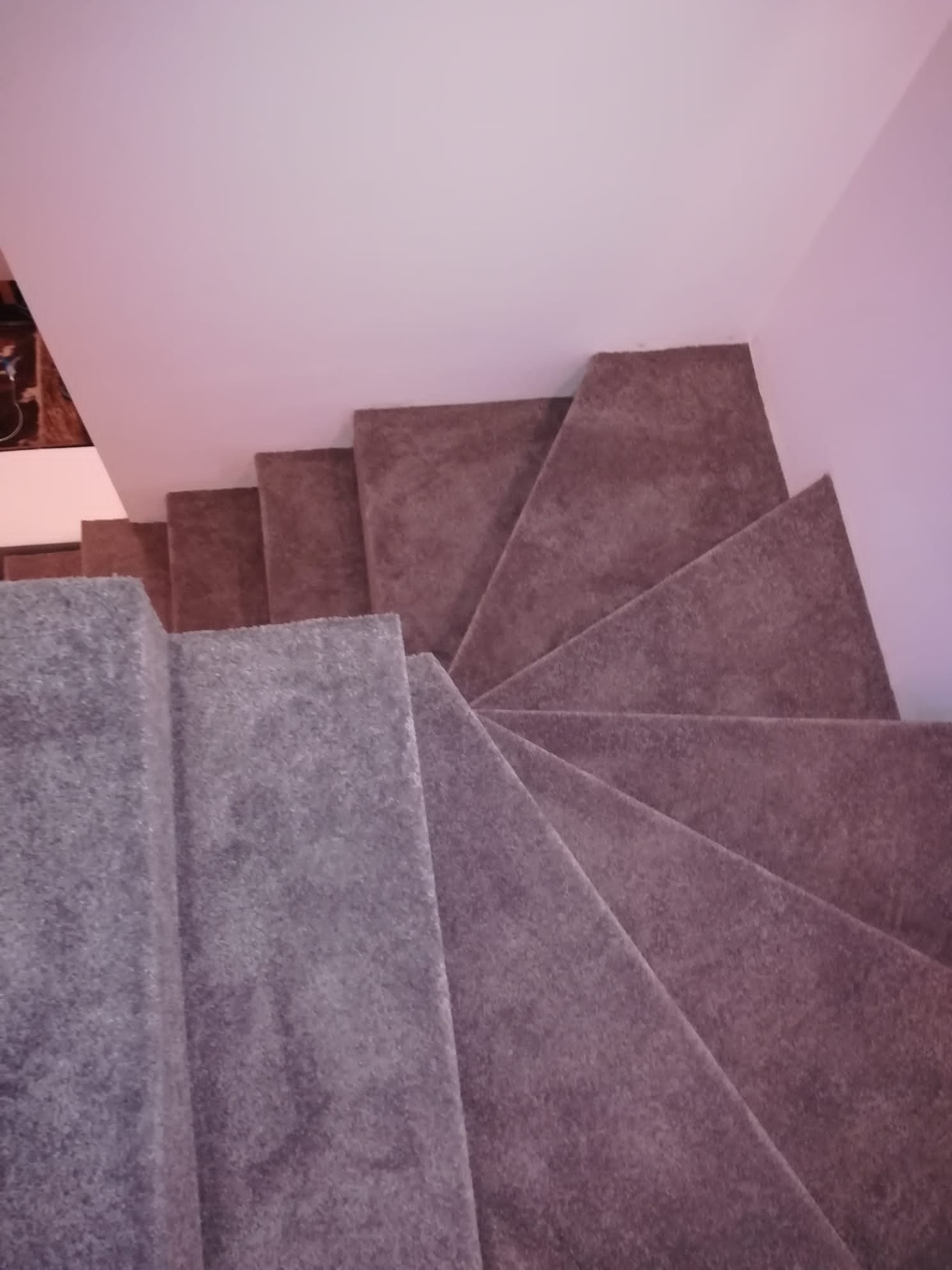 Widok z góry na schody pokryte szarą wykładziną dywanową, z widoczną strukturą materiału i załamaniem światła na stopniach.