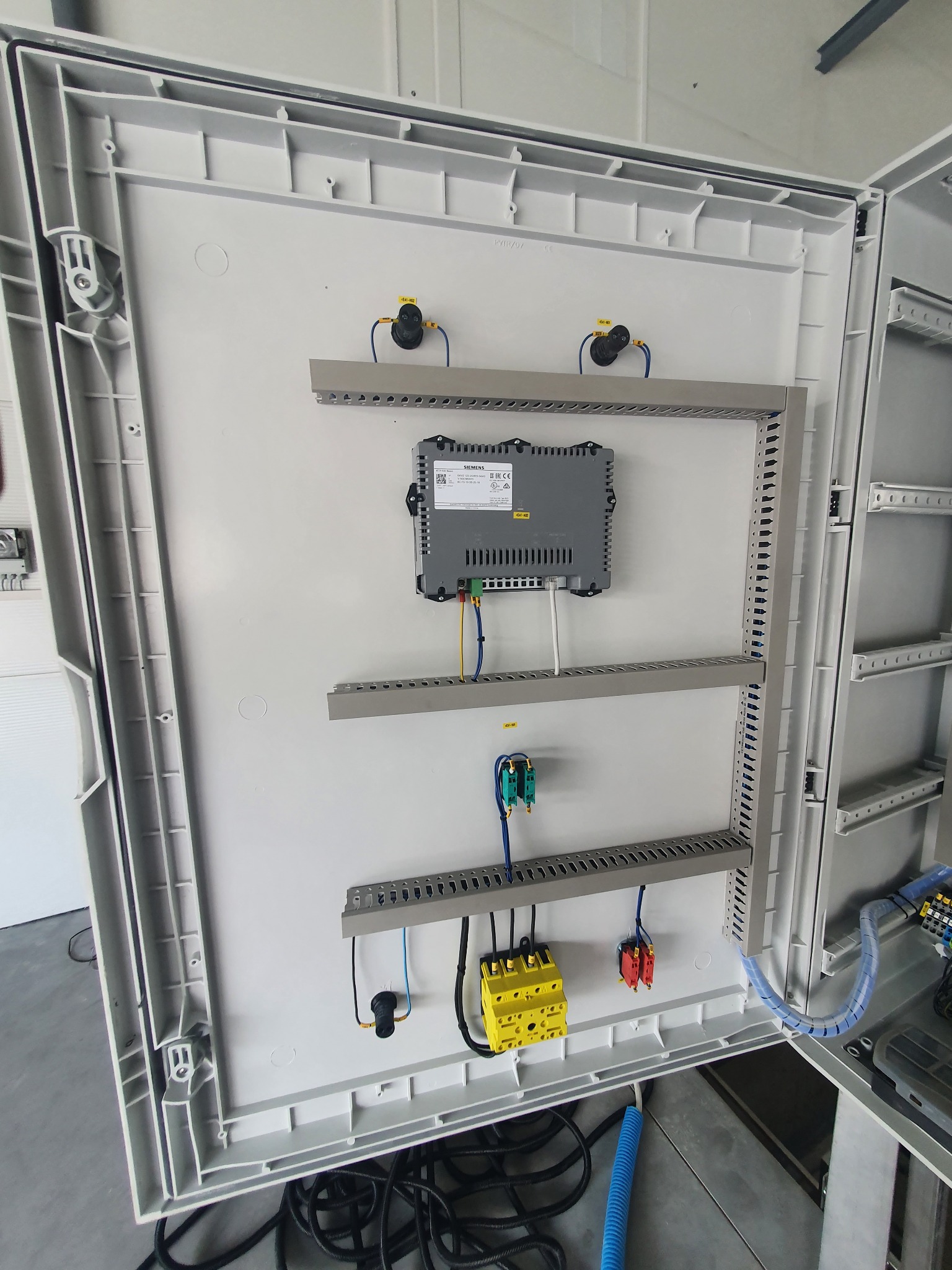 Otwarta skrzynka elektryczna z zamontowanym sterownikiem Siemens, bezpiecznikami i przewodami, widoczne szyny montażowe i elementy instalacji.