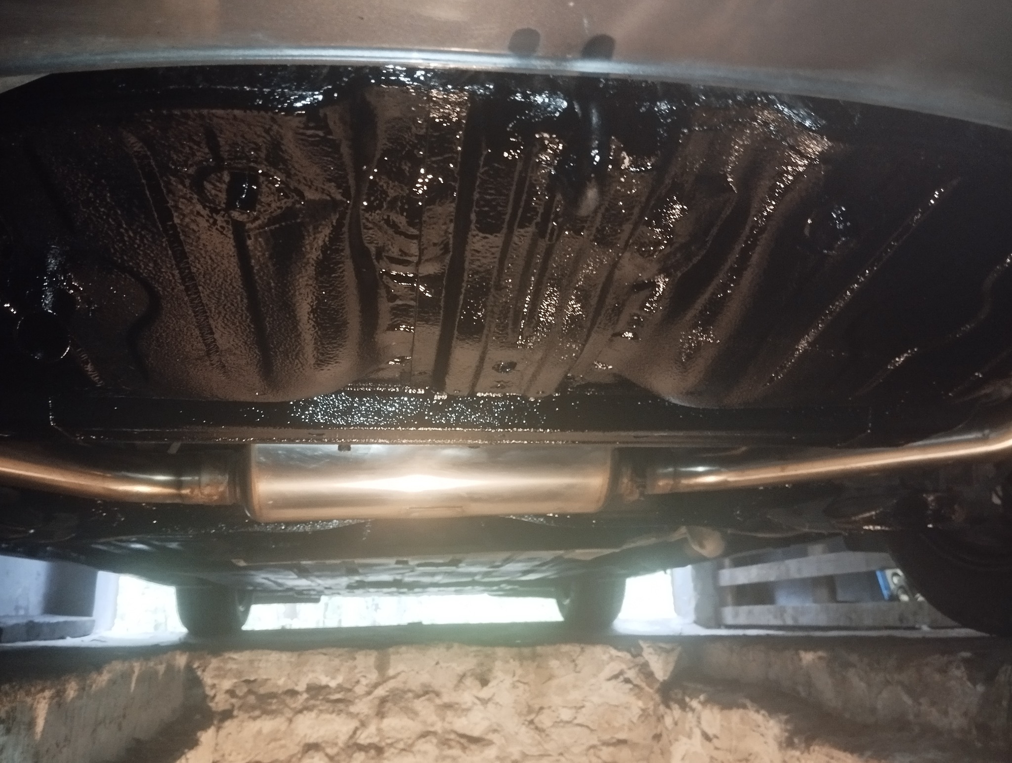 Podwozie auta po konserwacji antykorozyjnej, widoczny nowy układ wydechowy i zabezpieczone, błyszczące elementy. Auto na podnośniku.