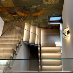Sun-Glass Michał Gregotowicz - Nowoczesne schody drewniane z balustradą ze szkła hartowanego, widok z góry, oświetlenie LED w stopniach, dekoracyjny kamień na suficie.