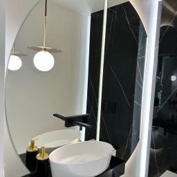 Sun-Glass Michał Gregotowicz - Nowoczesna łazienka z owalnym lustrem, czarnym blatem z umywalką nablatową i armaturą w kolorze czarnym, oświetleniem LED i czarnymi płytkami imitującymi marmur.