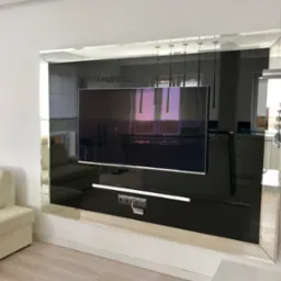 Nowoczesna ściana telewizyjna z lustrzanym obramowaniem, zrealizowana w Piastowie, odbijająca wnętrze salonu z sofą i oświetleniem.