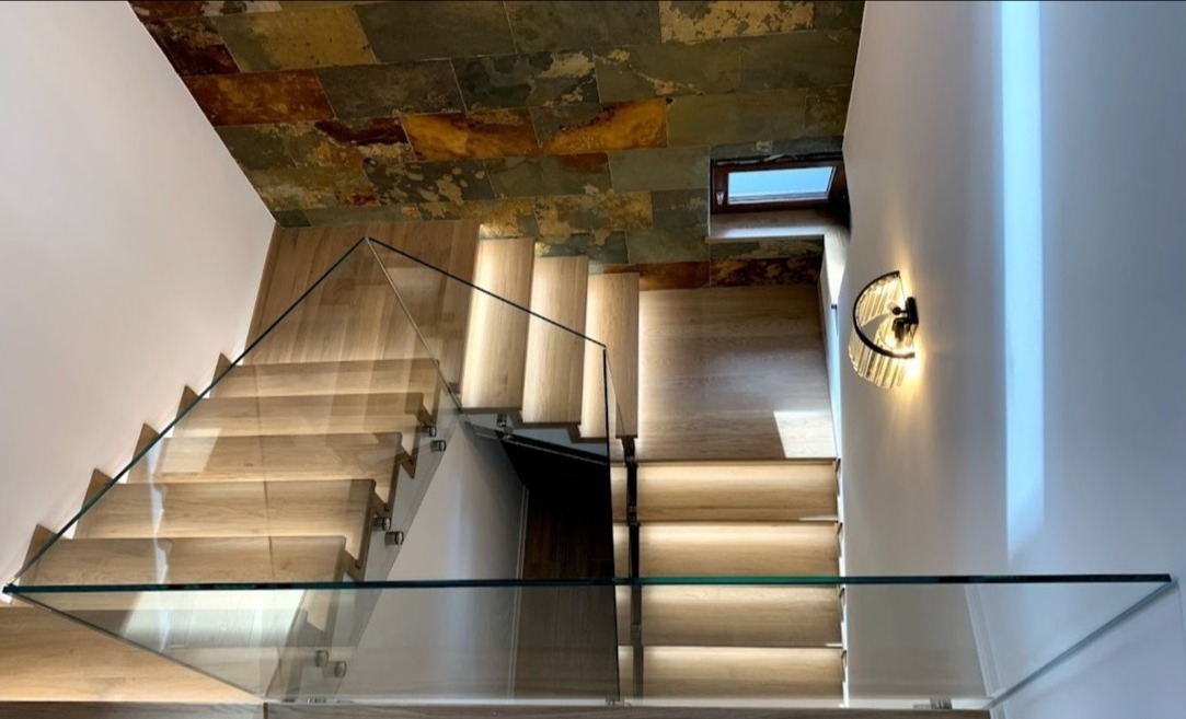 Nowoczesne schody drewniane z balustradą ze szkła hartowanego, widok z góry, oświetlenie LED w stopniach, dekoracyjny kamień na suficie.
