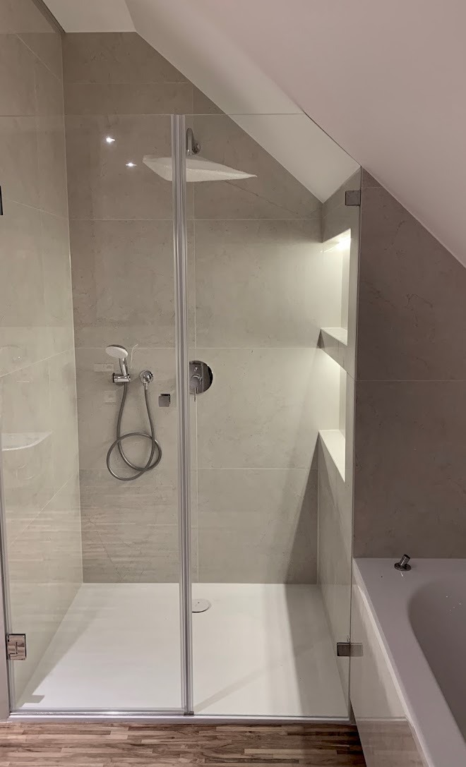 Nowoczesna kabina prysznicowa ze szklanymi drzwiami, zamontowana w łazience na poddaszu z wnękami oświetlonymi LED.