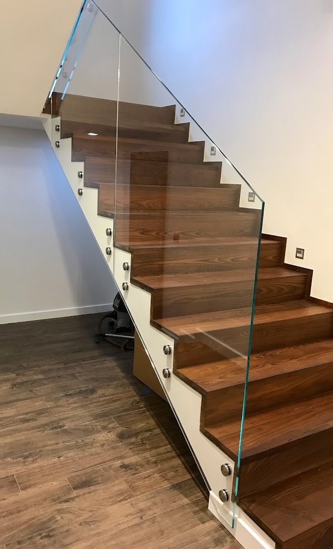 Nowoczesne schody z drewnianymi stopniami i szklaną balustradą mocowaną na metalowych uchwytach, oświetlenie w stopniach, widok z dołu na górę.