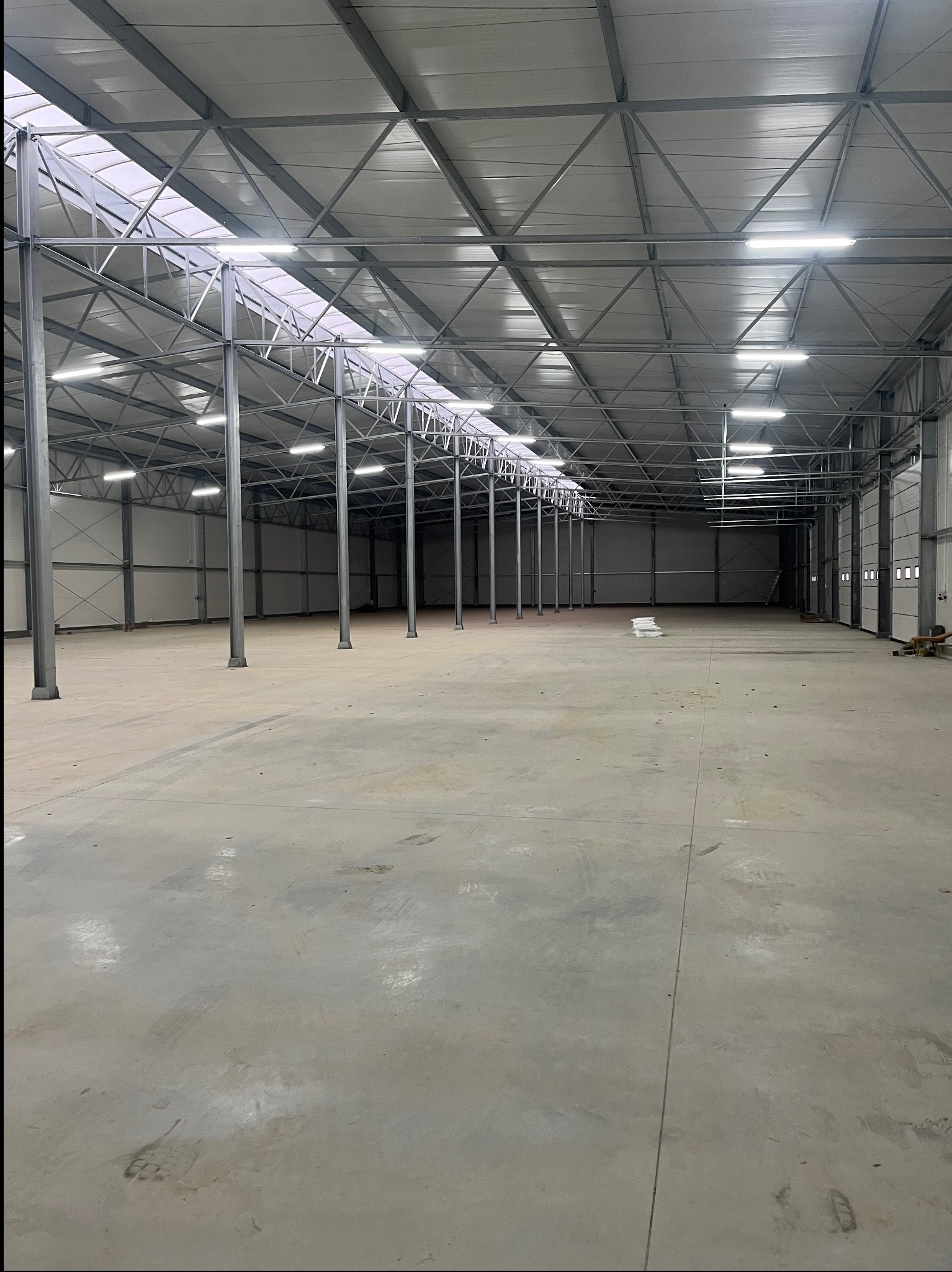 Wnętrze hali magazynowej z zamontowanym oświetleniem LED, widoczne metalowe słupy konstrukcyjne i świetliki w dachu.