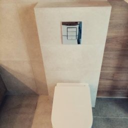 Twoje wymarzone mieszkanie - Nowoczesna toaleta podwieszana z chromowanym przyciskiem spłukującym, obudowana płytkami w odcieniach beżu i szarości, widok z góry.