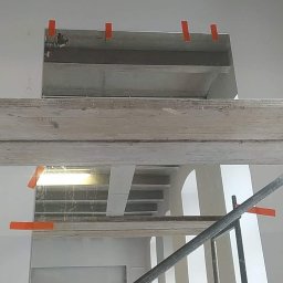 Twoje wymarzone mieszkanie - Sufit w trakcie prac, widoczne elementy konstrukcyjne i instalacje zabezpieczone pomarańczową taśmą, fragment rusztowania w kadrze, w tle widoczni dwaj mężczyźni.