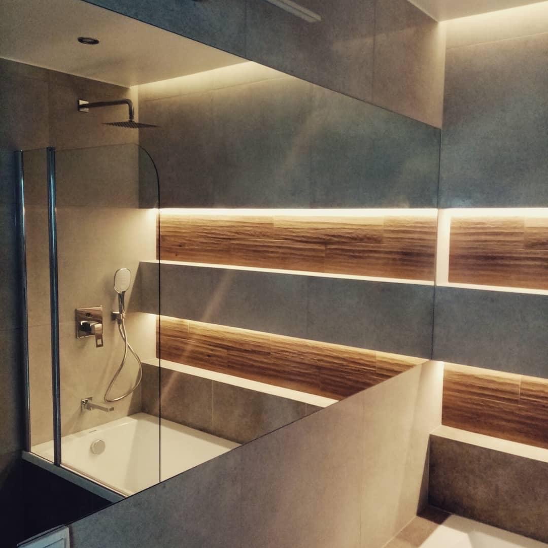 Nowoczesna łazienka z kabiną prysznicową, deszczownicą i podświetlanymi drewnianymi panelami na ścianie z szarych płytek.